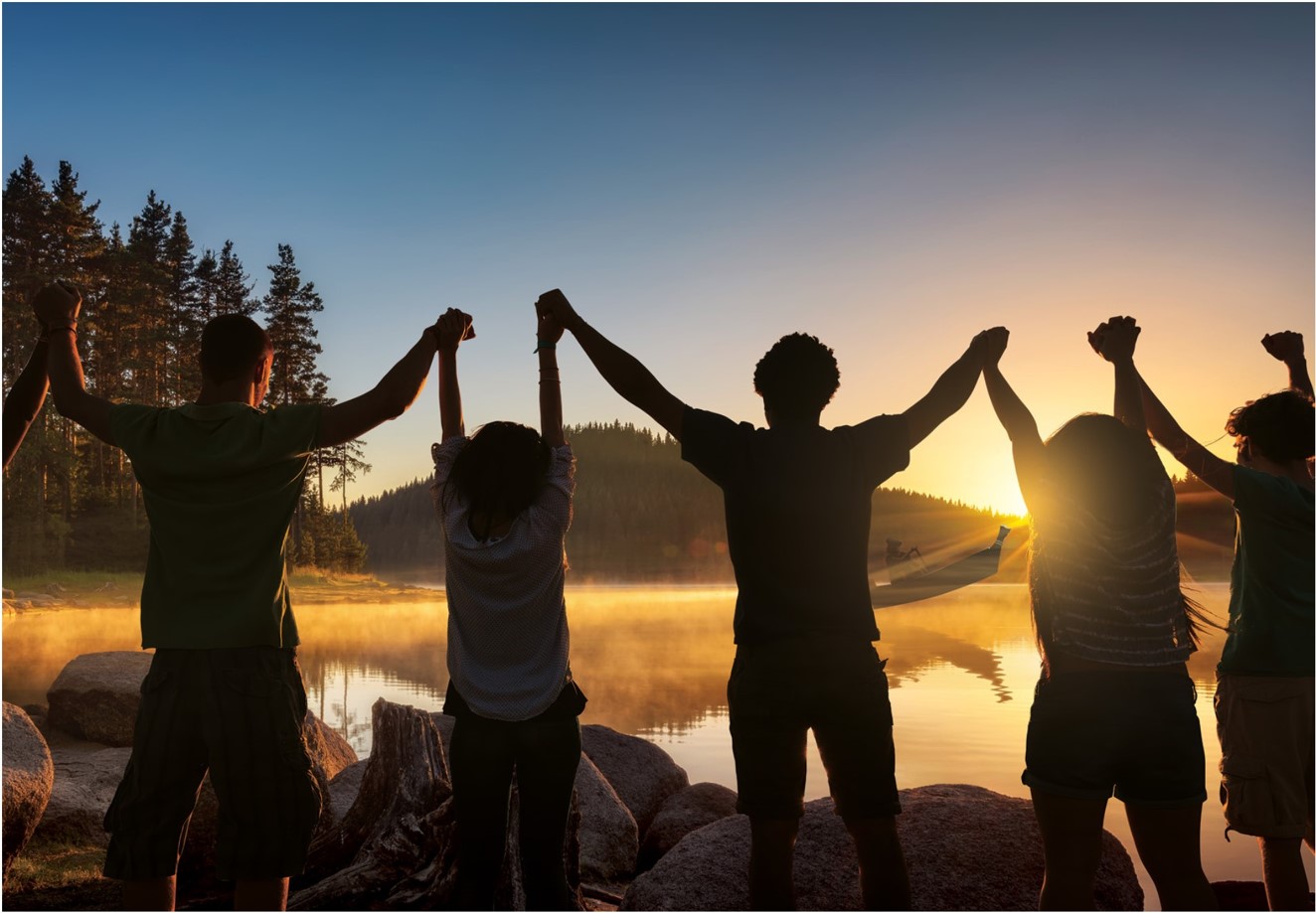 Children holding hands together above their heads at sunset by a lake.